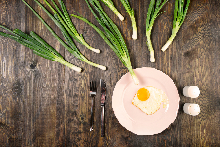 Assiette avec œuf au plat et oignons verts sur fond en bois — aliments riches en nutriments favorables à la fertilité.