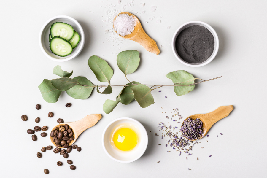 Ingrédients naturels pour le soin des cheveux maison : rondelles de concombre, huile, café, sel, argile, lavande et eucalyptus sur fond clair.
