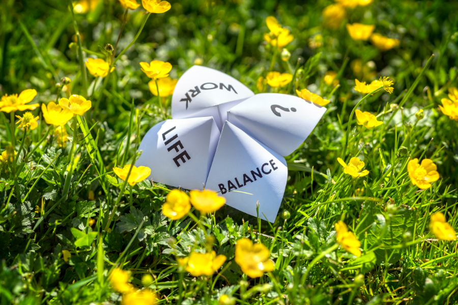 Qualité de vie au travail : Un origami “Work-Life Balance" posé dans un champ de fleurs jaunes, symbole du questionnement sur l’équilibre entre performance et bien-être
