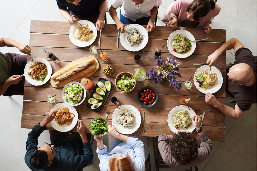 Personnes partageant un repas sain et varié autour d’une grande table, représentant le concept de manger en pleine conscience, écouter son corps et retrouver une relation saine à la nourriture.