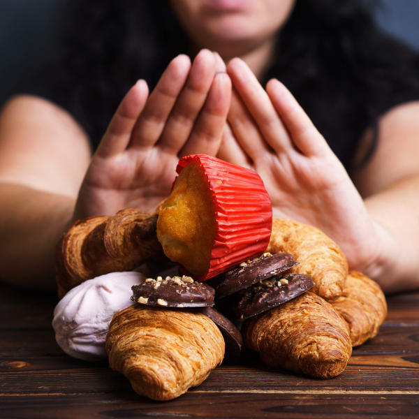 Personne refusant des viennoiseries et pâtisseries sucrées comme des croissants et biscuits, illustrant la volonté de réduire le sucre pour une meilleure santé et adopter des alternatives au sucre.