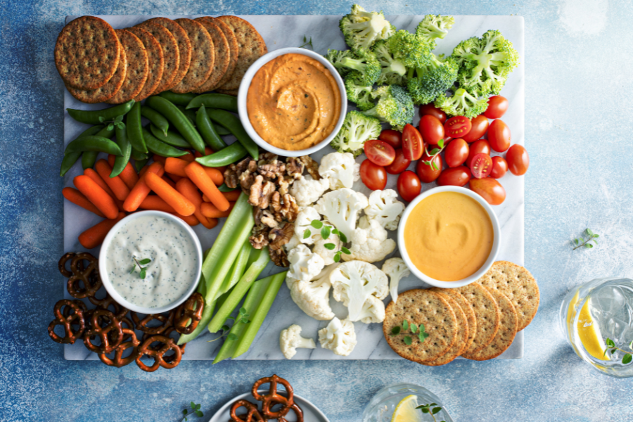 Plateau coloré de légumes frais, dips maison, noix, tomates cerises et crackers, illustrant une alimentation intuitive, équilibrée et respectueuse des besoins du corps.